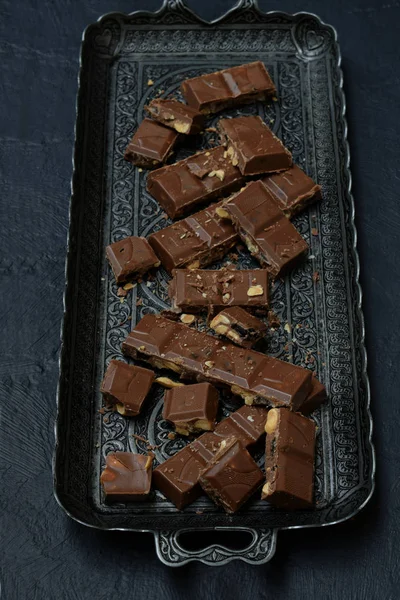 Chocolate com leite com nozes e frutas secas em uma bandeja de metal em um fundo de concreto escuro — Fotografia de Stock