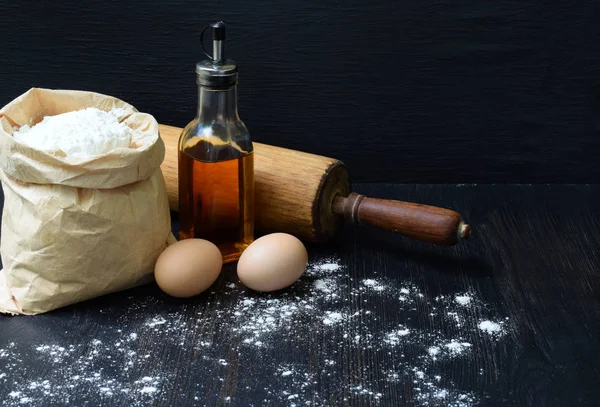 Táska, búzaliszt, tojás, olaj-és sodrófa összetétele. Felkészülés dagasztása tésztát, sütés a sötét háttér előtt. Hely a szöveg — Stock Fotó