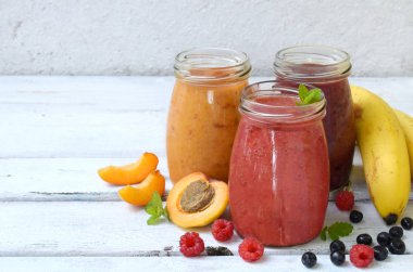 Turuncu, kırmızı ve mor sağlıklı smoothies taze malzemeler - muz, kayısı, ahududu ve hafif bir arka plan üzerinde yaban mersini. Kopya alanı
