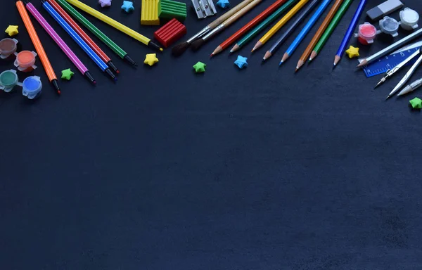 Accessori e forniture scolastiche: matite, pennarelli, vernici, penne, lavagna per iscrizioni su sfondo scuro. Torniamo a scuola. Vista dall'alto. Posa piatta — Foto Stock