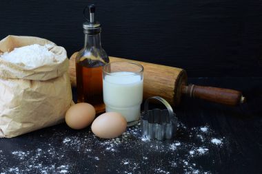 Buğday unu, yumurta, yağ, süt ve oklava torba bileşimi. Cookie koyu arka plan üzerinde pişirme hamur yoğurma için hazırlık. Metin için yer