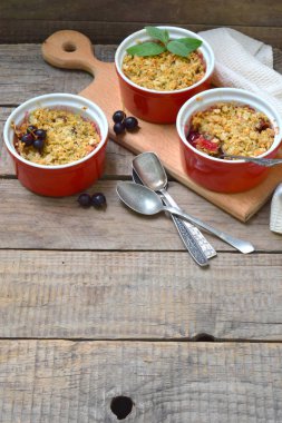 Meyve güveç ya da elma ve kahverengi Kupası ramekin ahşap arka plan üzerinde meyveleri ile kek. Uzay kopyalayın. Doğal ışık ile fotoğraf çekimi