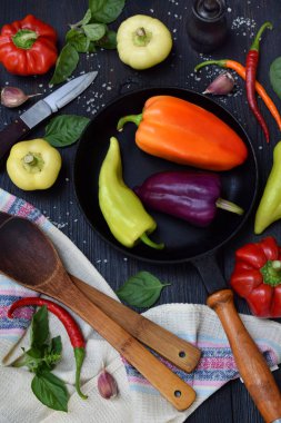 Tatlı ve sıcak biber koyu ahşap arka plan üzerinde farklı çeşitleri ile siyah bir kızartma tavası. Yahni veya kızartma hazırlanması. Kopya alanı