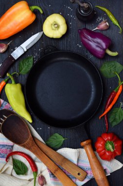 Bir boş siyah kızartma tavası, tatlı ve sıcak biber koyu ahşap arka plan üzerinde farklı çeşitleri çevresinde. Yahni veya kızartma hazırlanması.