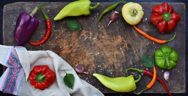 A frame for recipe from different varieties of sweet and hot pepper on a wooden background. Food border. Copy space
