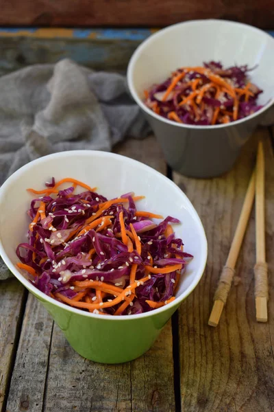 Salát z fialové nebo červené zelí a mrkev posypané sezamem na dřevěné pozadí. Zdravé a vegetariánská jídla — Stock fotografie