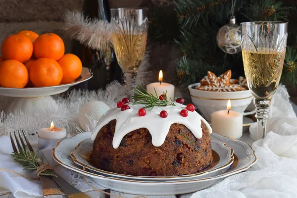 Traditioneller englischer Weihnachtspudding mit Winterbeeren, Trockenfrüchten, Nuss im festlichen Rahmen mit Weihnachtsbaum, brennender Kerze, Mandarinen und einem Glas Weißwein, Champagner. Obstkuchen — Stockfoto