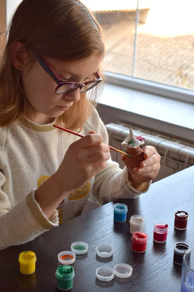 Girl making do-it-yourself toys, paints a pottery clay toy with gouache. Indoors creative leisure for children. Supporting creativity, learning by doing, DIY project, hand craft. Master class of art.