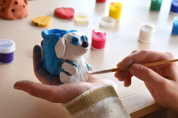 Facendo giocattoli, dipinge una figura di cane di argilla di ceramica con guazzo. All'aperto tempo libero creativo per i bambini. Sostenere la creatività, imparare facendo, progetto fai da te, artigianato. Master class d'arte . — Foto Stock