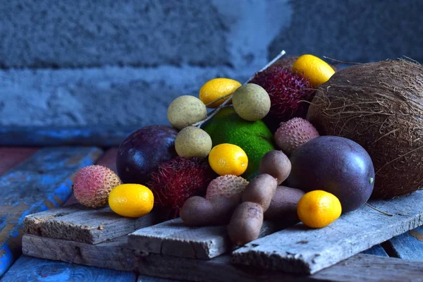 Mix z dojrzałych owoców tropikalnych z marakui, kumkwat, liczi, rambutan, tamaryndowca, awokado, kokos, oko smoka na podłoże drewniane. Tło pożywienie. Potrawy wegetariańskie — Zdjęcie stockowe