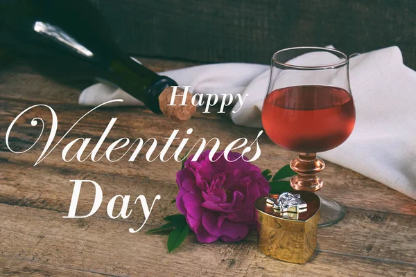 Un bicchiere di vino rosso, bottiglia e rosa sul tavolo in legno rustico. La natura morta di San Valentino. Concetto biglietto di auguri con l'iscrizione Buon San Valentino. Copia spazio per testo — Foto Stock