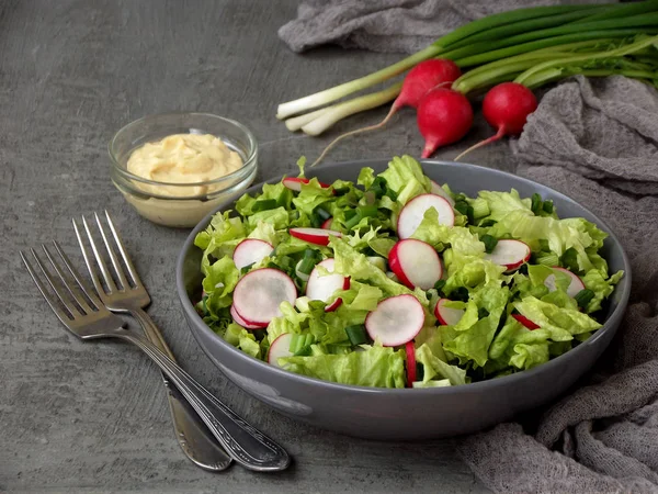 Vitamin salad from lettuce, radish, green onions and eggs, seasoned with vegetable oil and mustard in plate on gray concrete background. Healthy food