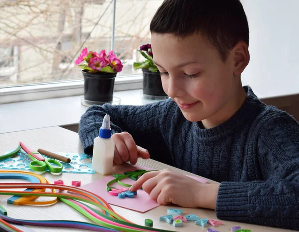 Técnica de Quilling. Niño haciendo decoraciones o tarjeta de felicitación. Tiras de papel, flores, tijeras. Artesanía artesanal en días festivos: Cumpleaños, Día de la Madre o del Padre, 8 de marzo, Boda. Concepto DIY para niños . —  Fotos de Stock