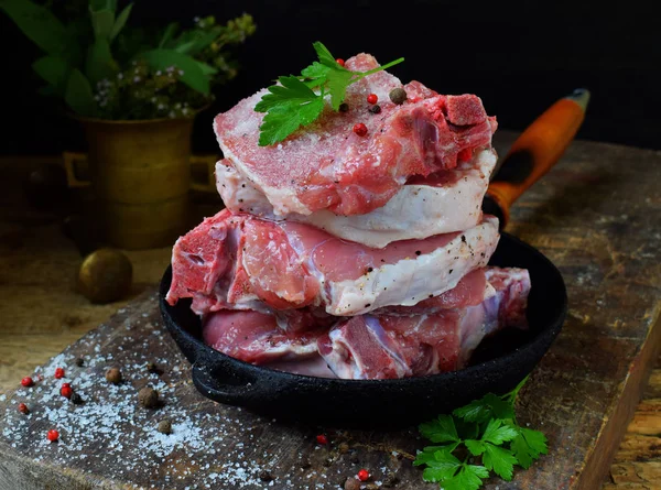 Carne cruda di maiale cosparsa di pepe nero macinato, sale e spezie in una padella di ghisa su fondo di legno. Preparazione per bistecca, arrosto, stufato. Spazio per testo . — Foto Stock