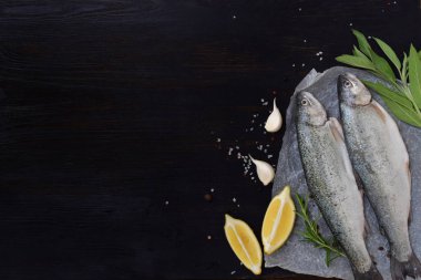 İki nehir alabalığı otlar, baharatlar, limon ve biber ahşap tahta üzerinde bir gemide yemek pişirmek için hazır. Taze balık.