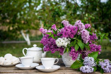 Ahşap arka planda vazoda leylak çiçekleri. Kahvaltı saatinde masada çay fincanı.
