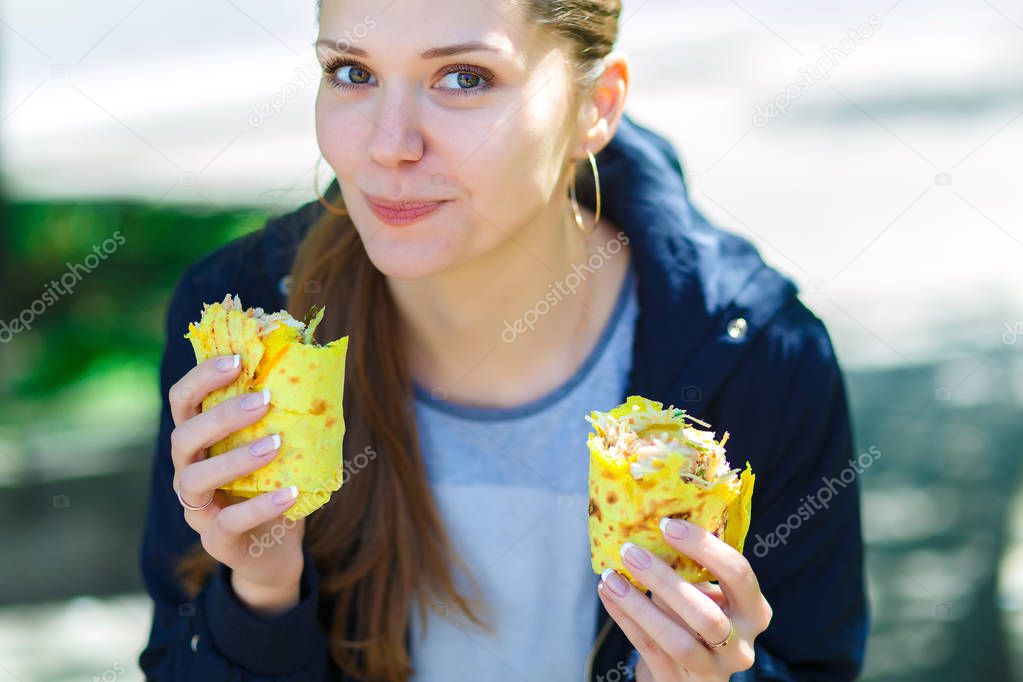 The girl eats shawarma on the street.