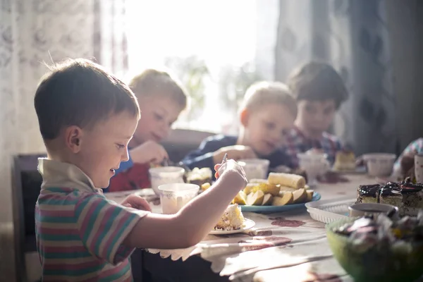 Kinderen zitten aan de tafel met vruchten, thee, snoep en taart — Stockfoto