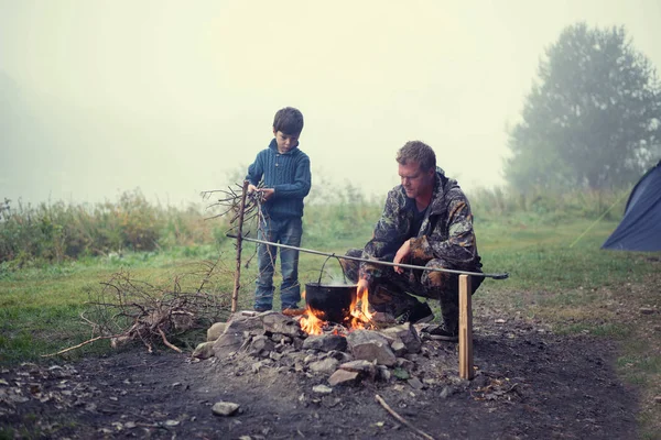 Vater und Sohn auf dem Fluss am Feuer. — Stockfoto