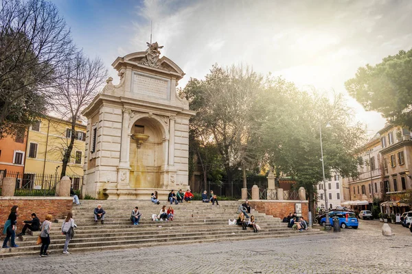 Unkenntliche menschen, die auf den treppen unter dem monumentalen marmorbrunnen auf der historischen piazza trilussa im berühmten viertel trastevere in rom sitzen — Stockfoto