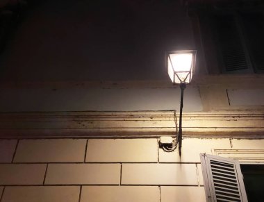 Roma 'nın tarihi merkezindeki eski bir binanın duvarına dikilmiş antik dövmeli demir sokak lambası.