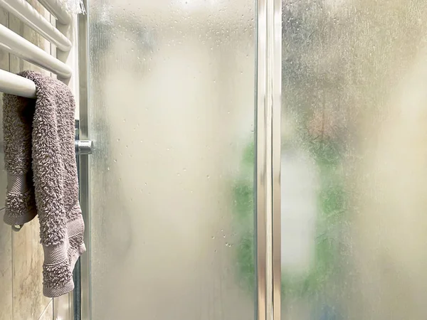 Fialový ručník umístěný na bílém radiátoru v blízkosti sprchového koutu s matnými skleněnými dveřmi a hliníkovou konstrukcí uvnitř koupelny — Stock fotografie
