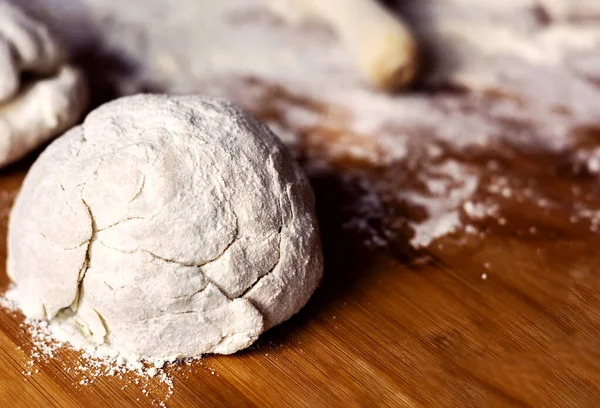 a dough on a flour-soiled wooden board with a blurred rolling pin. Preparation of flour-based foods before being baked