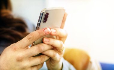 Beyaz tenli, genç bir kadının elleri dokunmatik ekranda akıllı bir telefon tutarken. Teknoloji ve mobil bağlantı.