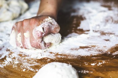Kadın eli un hamurunu tahta bir tahtaya yuvarlayarak yoğuruyor. Ekmek ya da pizza gibi un bazlı yiyeceklerin hazırlanması