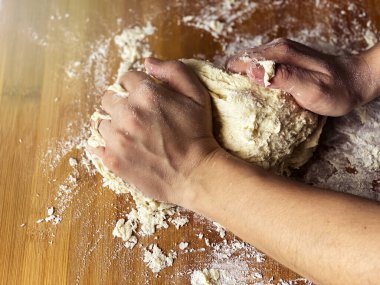 Kadın eli un hamurunu tahta bir tahtaya yuvarlayarak yoğuruyor. Ekmek ya da pizza gibi un bazlı yiyeceklerin hazırlanması. Ev mutfağı. Tahta masaya saçılmış un tozu.