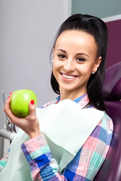 Mulher bonita paciente na cadeira dental sorrindo com maçã verde — Fotografia de Stock