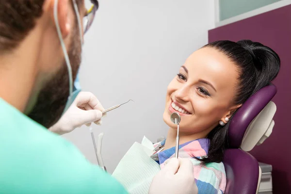 Mujer sentada en silla dental mientras el médico examina sus dientes —  Fotos de Stock