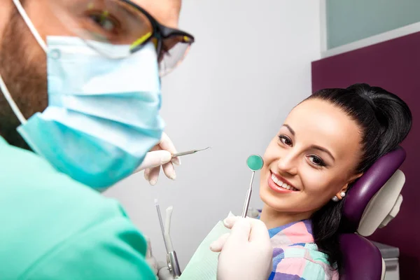 Mujer sentada en silla dental mientras el médico examina sus dientes —  Fotos de Stock