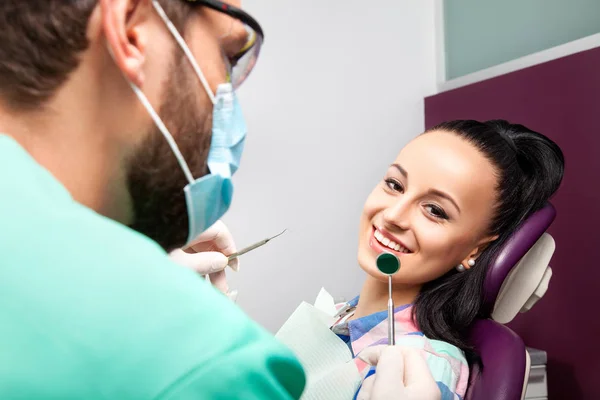 Mulher sentada na cadeira dentária enquanto médico examinando seus dentes — Fotografia de Stock