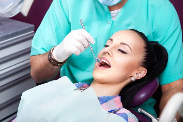 Mulher sentada na cadeira dentária enquanto médico examinando seus dentes — Fotografia de Stock
