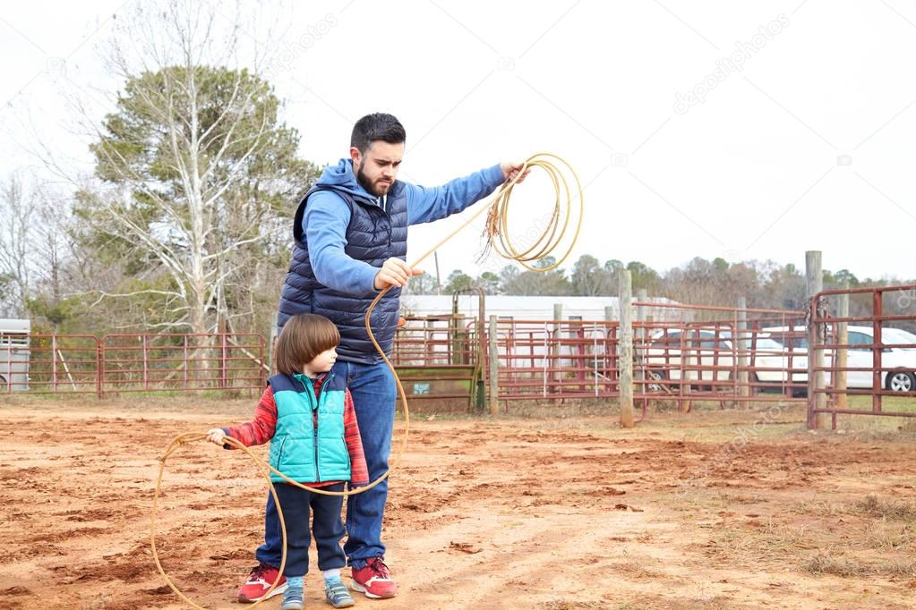 Father learning son making loop and throwing lasso in ranch