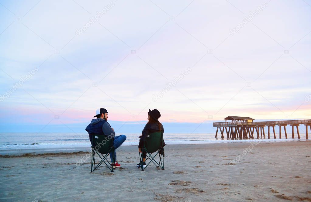 Couple sitting in deck chairs at beautiful sunset beach