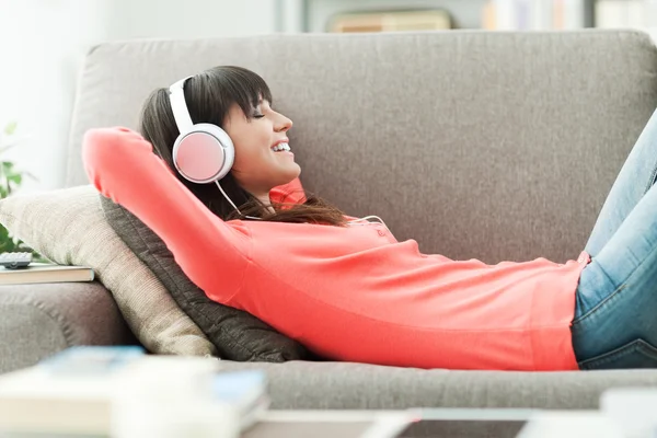 Ung attraktiv kvinna avkopplande i soffan hemma, hon lyssnar på musik med hörlurar — Stockfoto