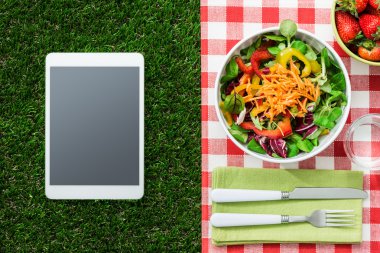 Taze sağlıklı salata ve çim, piknik ve sağlıklı beslenme kavramı üzerinde dijital tablet