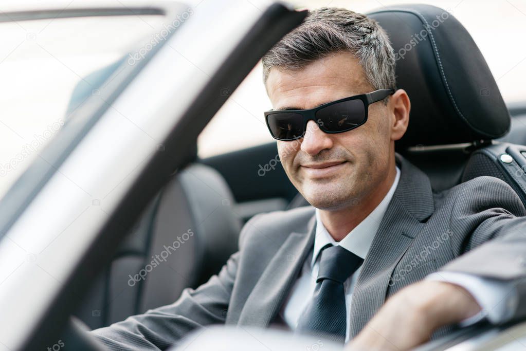 Successful confident businessman sitting in his brand new convertible car