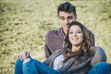 Çimenlerin üzerinde oturan gülümseyen genç Çift