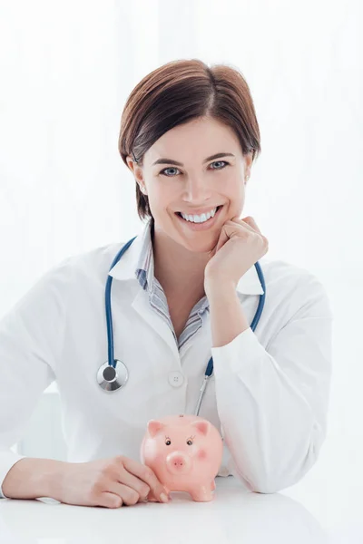 Female doctor and piggy bank: health insurance — Stock Photo, Image