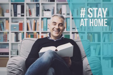 Gülümseyen adam kitap okuyor ve evde tek başına dinleniyor: Coronavirus önleme için sosyal medya kampanyasında evde kalın