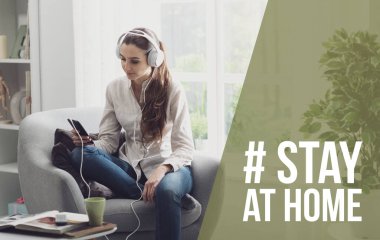 Oturma odasında dinlenen ve akıllı telefonuyla online müzik dinleyen genç kadın: Coronavirus önleme için sosyal medya kampanyasında evde kalın