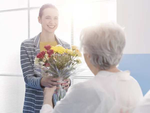 Усміхнена Молода Жінка Відвідує Бабусю Лікарні Дарує Квіти — стокове фото