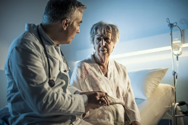 Caring doctor comforting a senior patient at the hospital at night, senior care concept