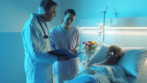 专业医疗小组在一位躺在病床上的老年病人旁边讨论 — 图库照片