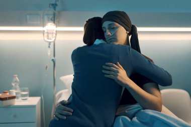 Kanserli arkadaşını rahatlatan ve destekleyen bir kadın. Yatakta oturup sarılıyorlar.