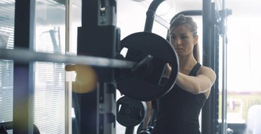 Spor salonunda atletik formda bir kadın halter kaldırıyor ve ağırlık çalışması yapıyor. Spor için halter hazırlıyor.