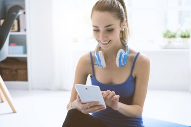 Kulaklıklar ile mutlu sportif kadın, o onun dijital tablet kullanarak çevrimiçi müzik arama